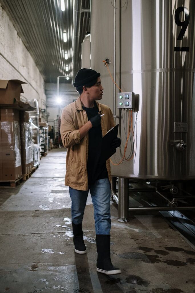 Man in brown jacket checking brewery tanks inside an industrial plant.