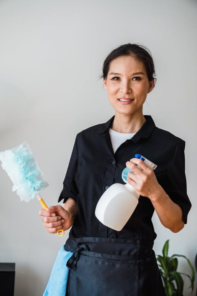 A female housekeeper smiling while holding cleaning tools indoor.